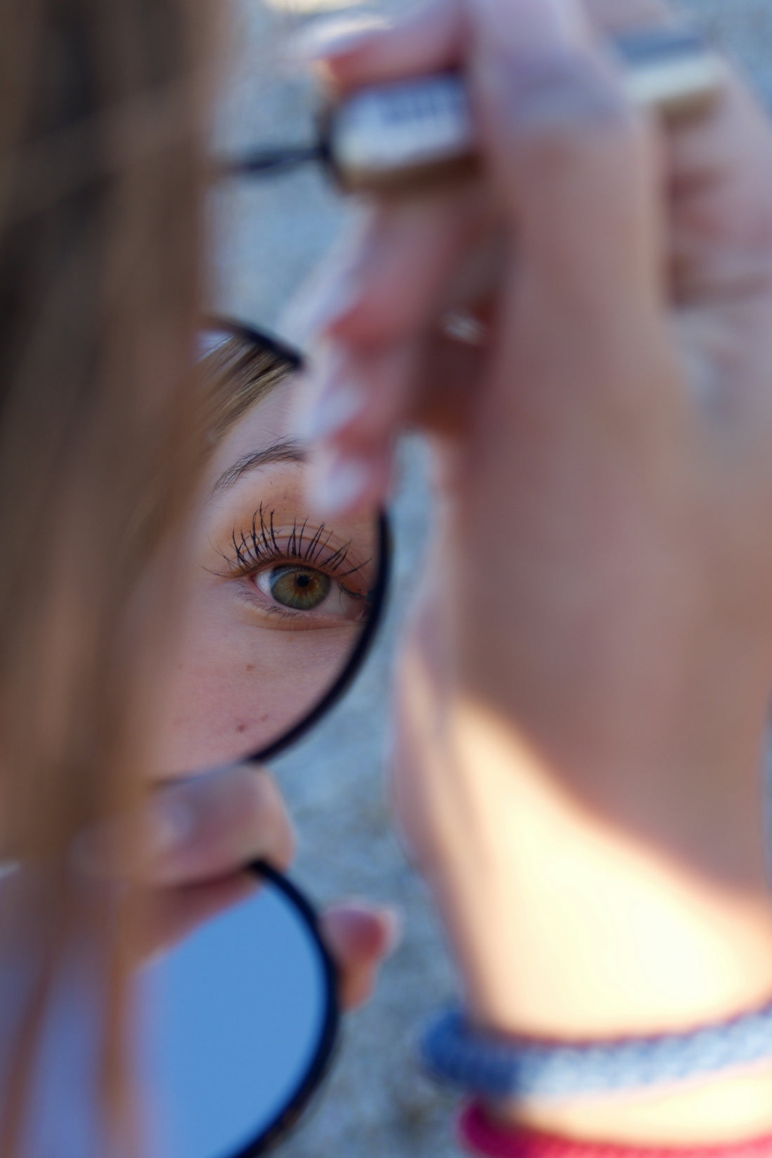 Person applying mascara, reflected in a small mirror
