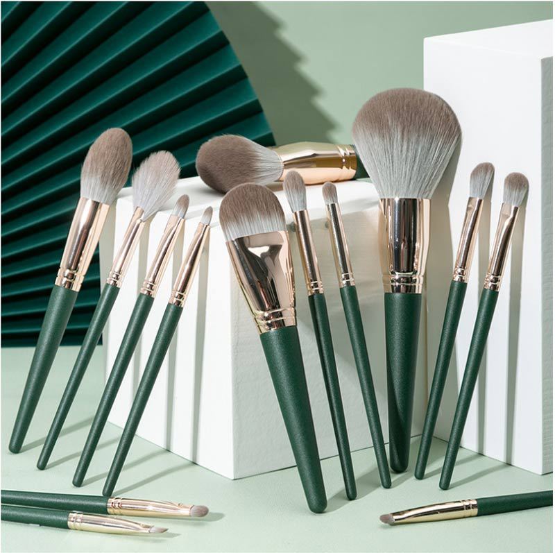 Set of makeup brushes with green handles and gold accents on a light green background